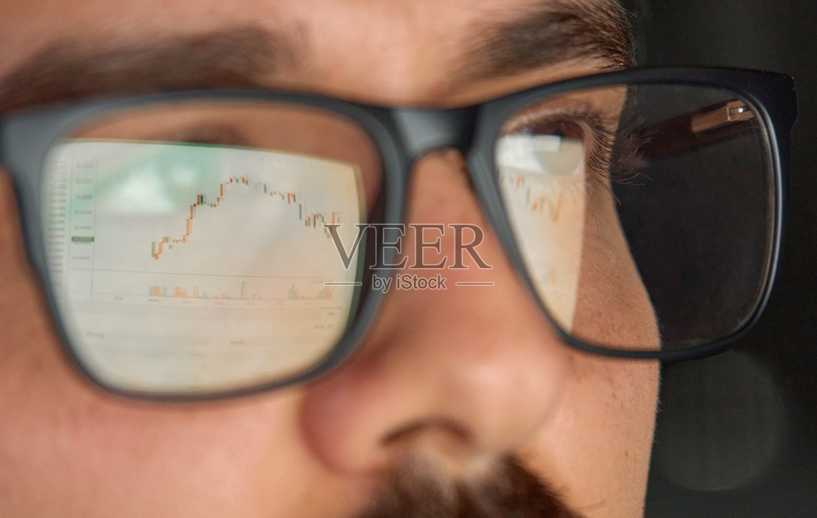戴眼镜的交易员、经纪人或投资者正在分析股票交易市场,眼镜上带有反光。照片摄影图片