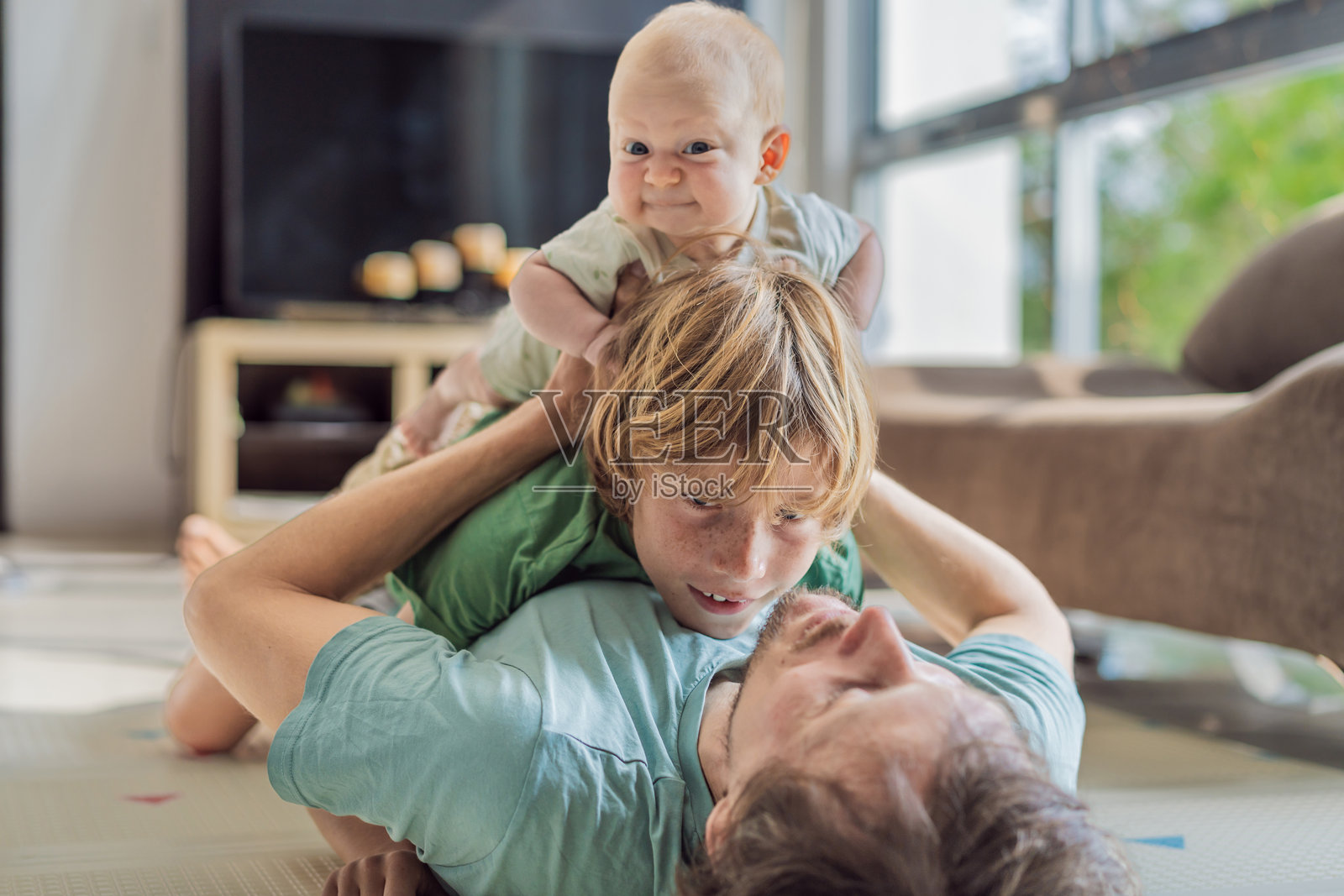 父亲、儿子和新生儿躺在地板上,在温馨的育婴室里庆祝新家庭成员的到来。为人父母、亲子关系和家庭之爱的概念照片摄影图片