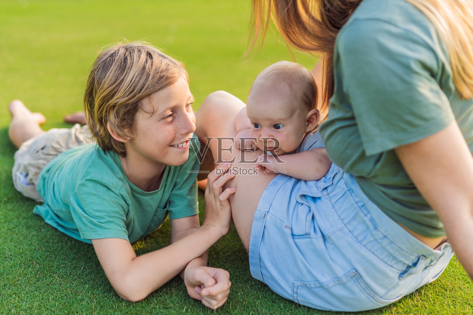 母亲、大儿子和新生儿在公园的草地上。一家人在大自然中享受亲子时光。父母之爱,爱与家庭纽带的概念照片摄影图片