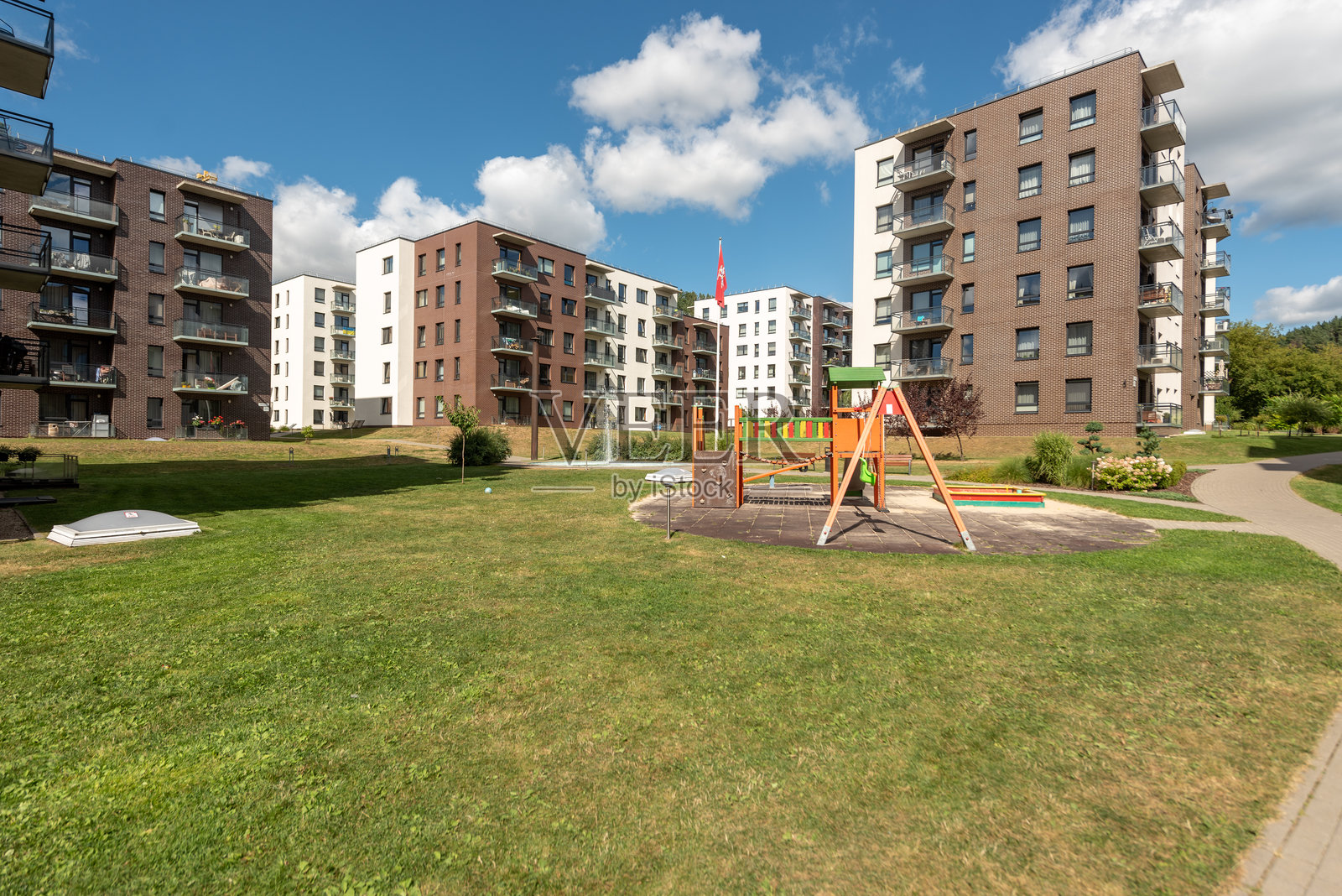 阳光明媚的日子里,现代住宅楼配有游乐场和绿色庭院照片摄影图片