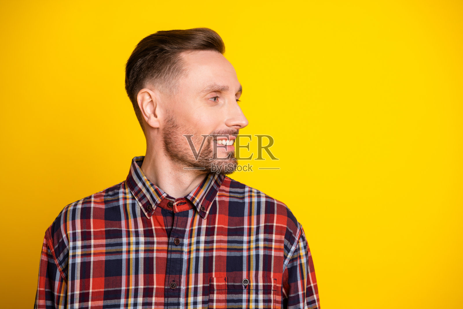 身穿格子衬衫的年轻男子对着镜头微笑,背景为明亮的黄色,适合用于广告和生活方式的休闲时尚肖像图库素材照片摄影图片