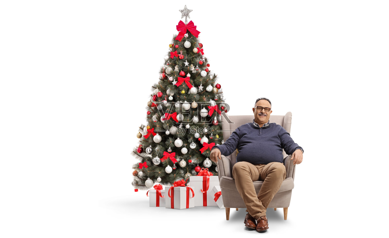 快乐的中年男子坐在扶手椅上,旁边是圣诞树,脸上带着笑容照片摄影图片
