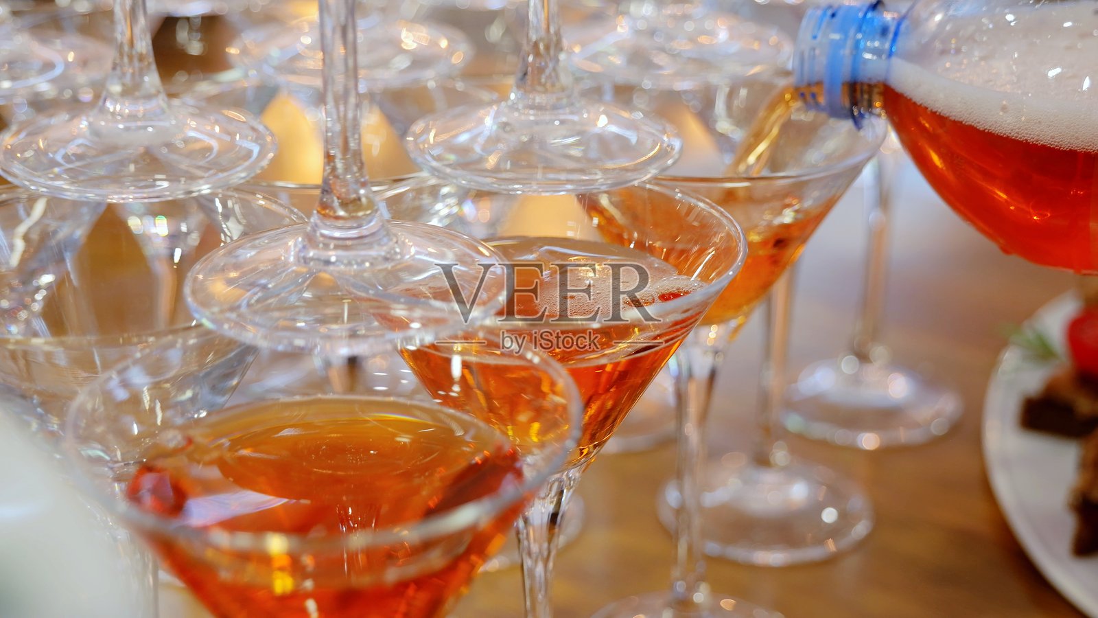 专业调酒师将色彩鲜艳的橙色鸡尾酒倒入叠放的酒杯中,在酒吧或活动现场以动感的酒品展示营造出节日的庆祝氛围照片摄影图片