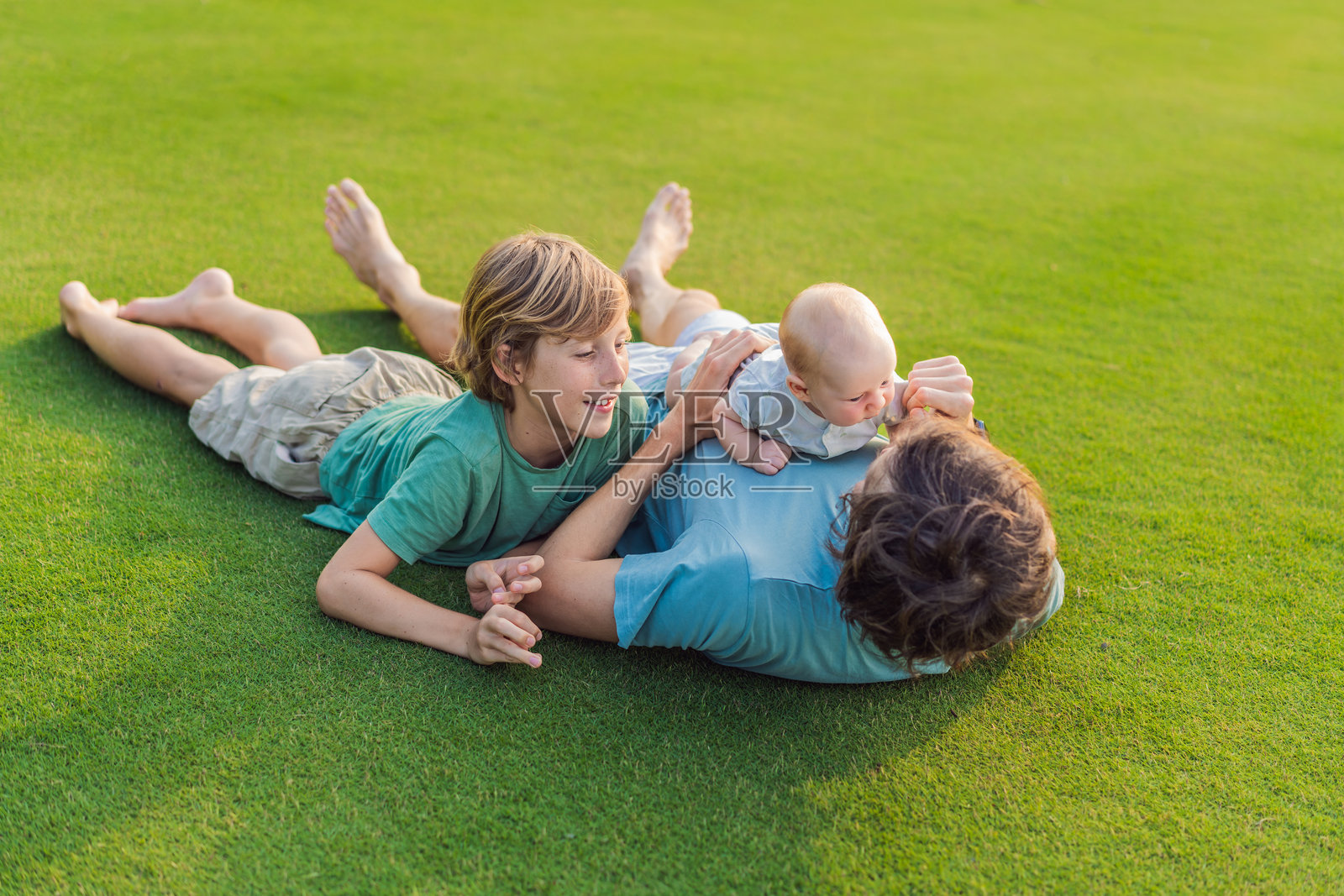 父亲、大儿子和新生儿在公园的草地上。一家人在大自然中享受亲子时光。父母之爱、亲情羁绊的概念。照片摄影图片