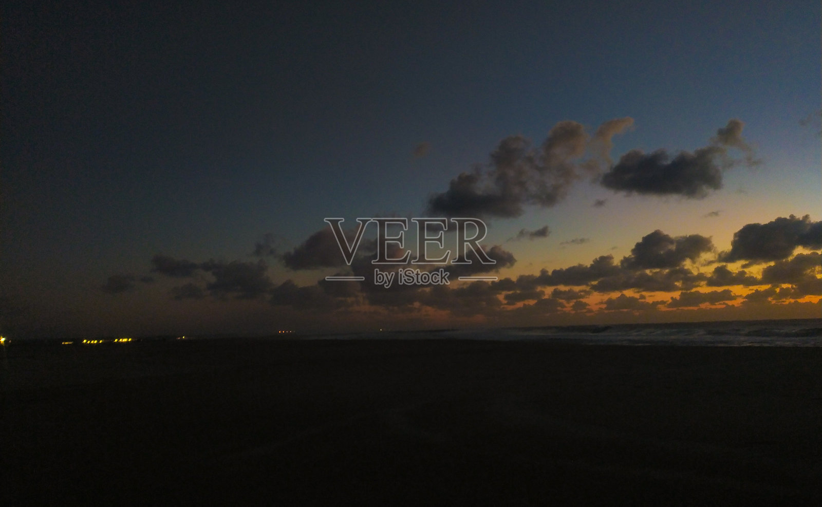 迷人的日落,笼罩着深邃海岸边的沙滩,伴有蓬松的云朵。金色的地平线融入了深蓝色的暮色天空,为旅行或冥想项目提供了宁静而富有氛围的场景。照片摄影图片