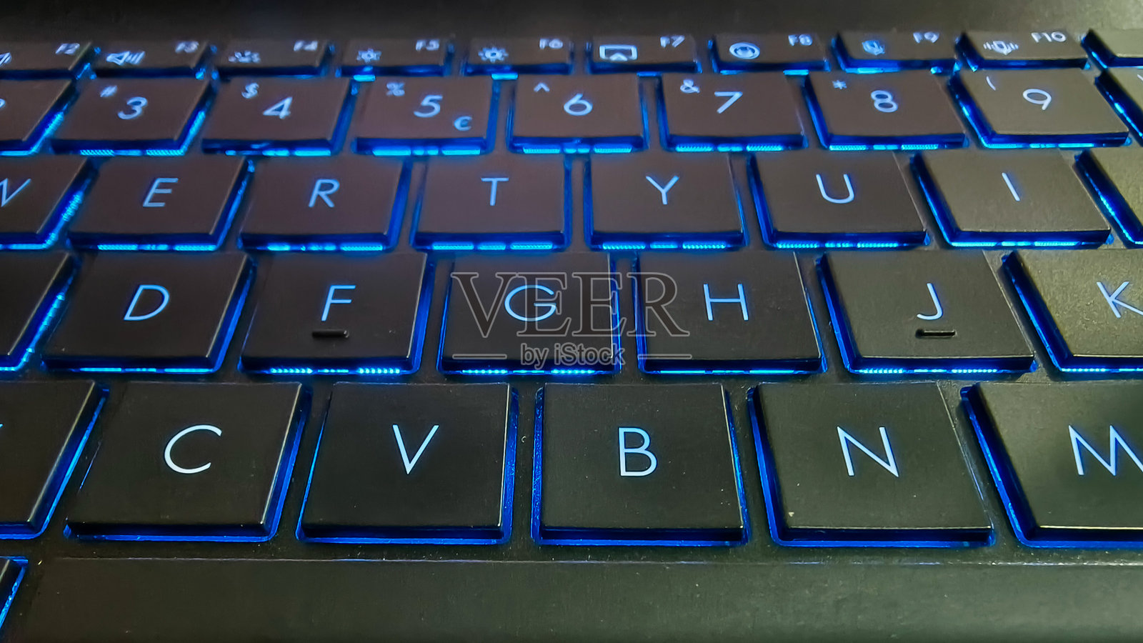 黑暗中笔记本电脑键盘的蓝色背光特写照片摄影图片