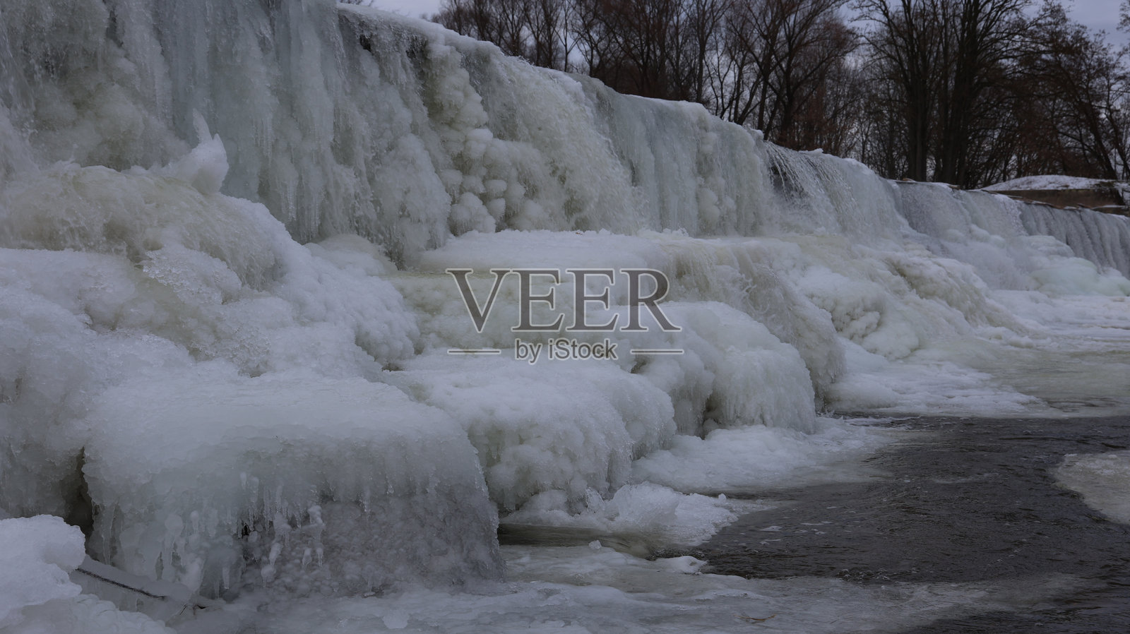 捷克Cvrcovice的冰封堰坝。寒冷冬日日落时,伊赫拉瓦河上的巨大冰层、冰柱和流淌的河水。照片摄影图片