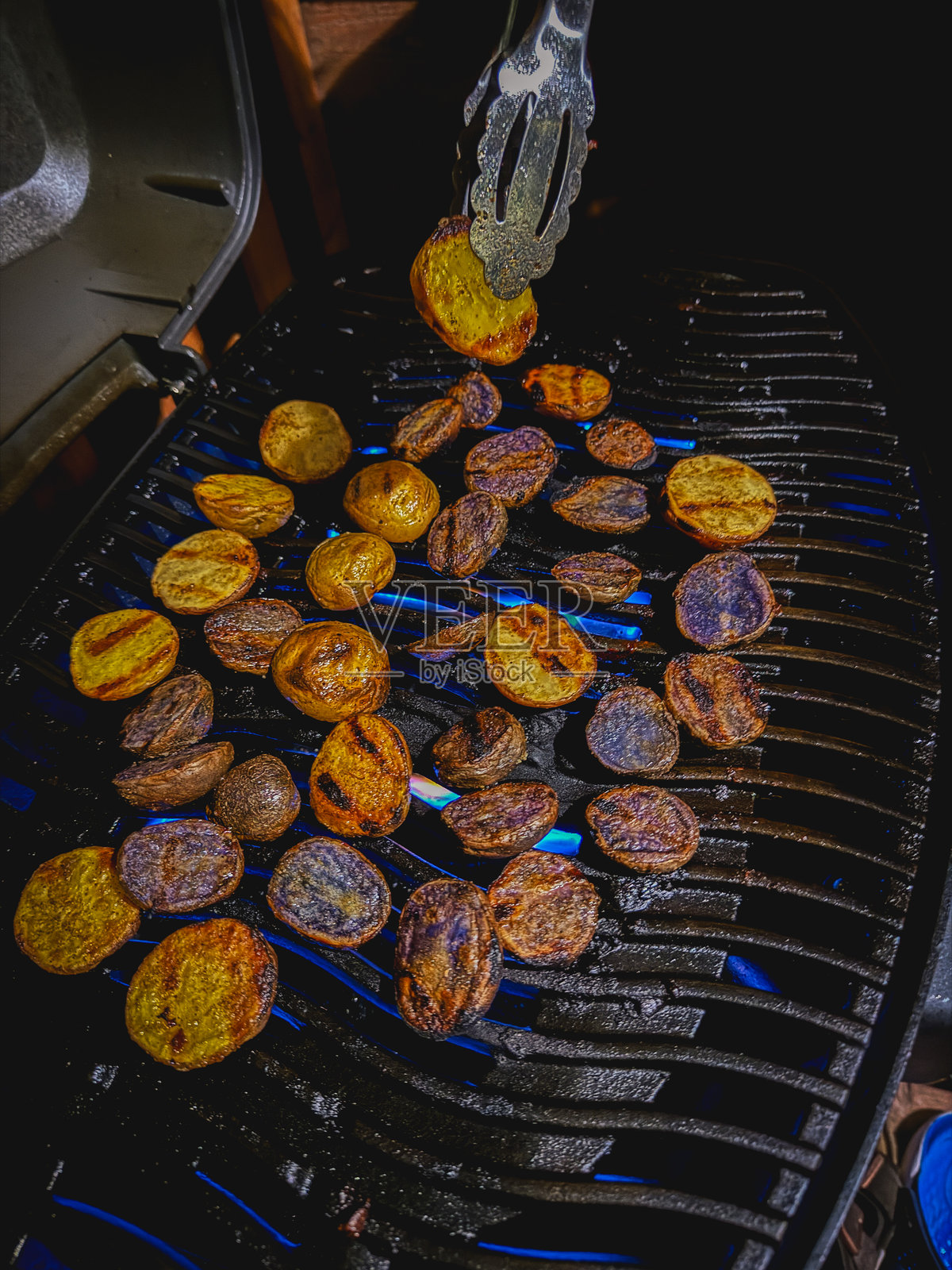 烧烤夹翻动烤架上色彩缤纷的土豆片照片摄影图片