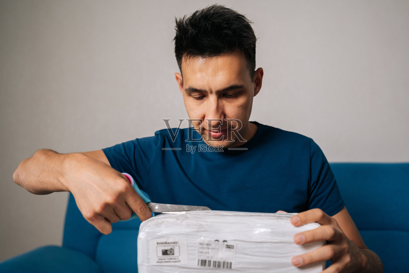 一名男性顾客在客厅里,坐着,用剪刀拆开包裹着电脑硬件的塑料包装。照片摄影图片