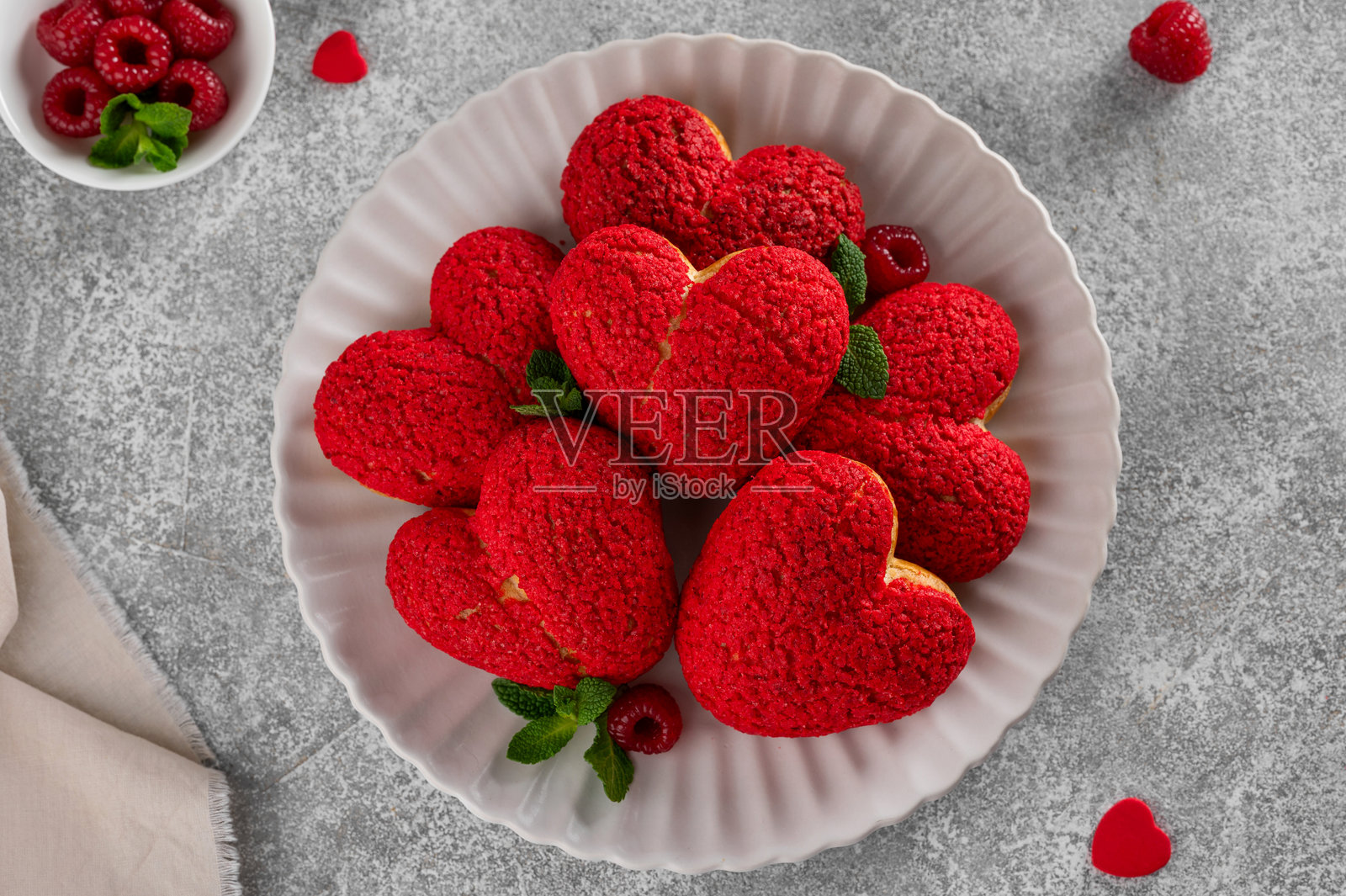 心形泡芙配红色闪电脆皮和覆盆子奶油——情人节甜点,摆放在盘子里,背景为混凝土。俯视角度,留有复制空间。照片摄影图片