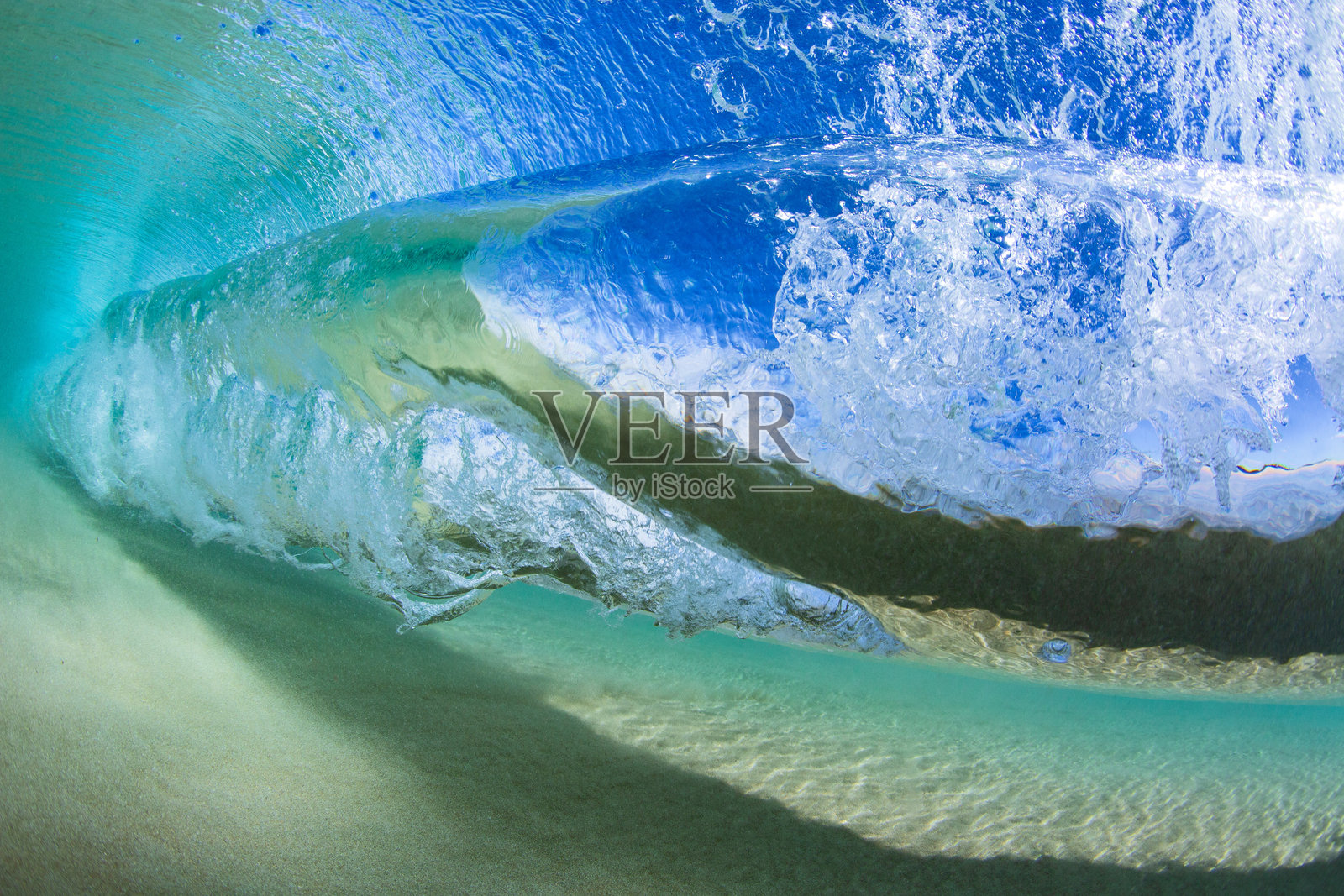 一只纹理优美的蓝绿色海浪在沙滩边翻卷破碎。从水下拍摄,水晶般清澈的浅水区,靠近沙滩海岸线。照片摄影图片