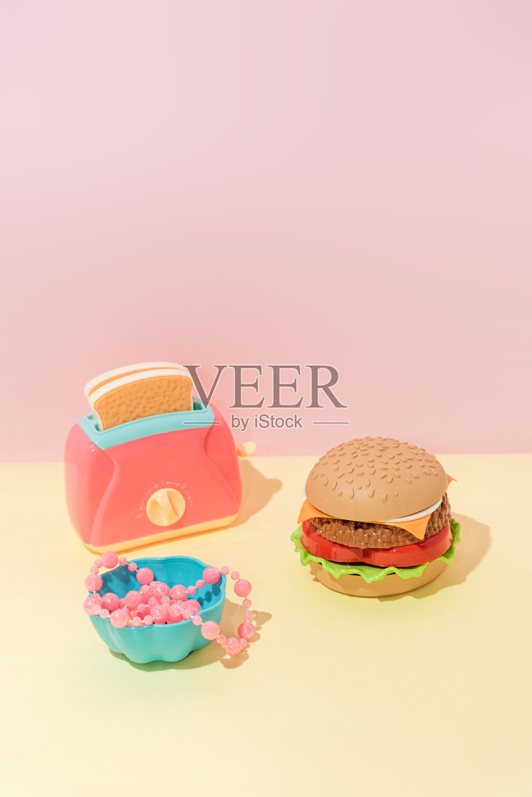 粉黄色背景上的创意汉堡、吐司和带珠子的静物盘照片摄影图片