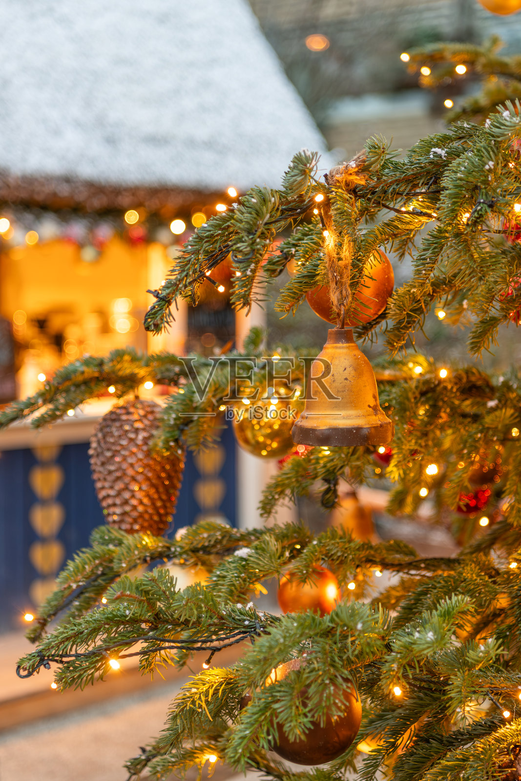特写:美丽的圣诞装饰、彩球和圣诞铃铛挂在蒂沃利公园的真松树上。背景中模糊的小房子。照片摄影图片