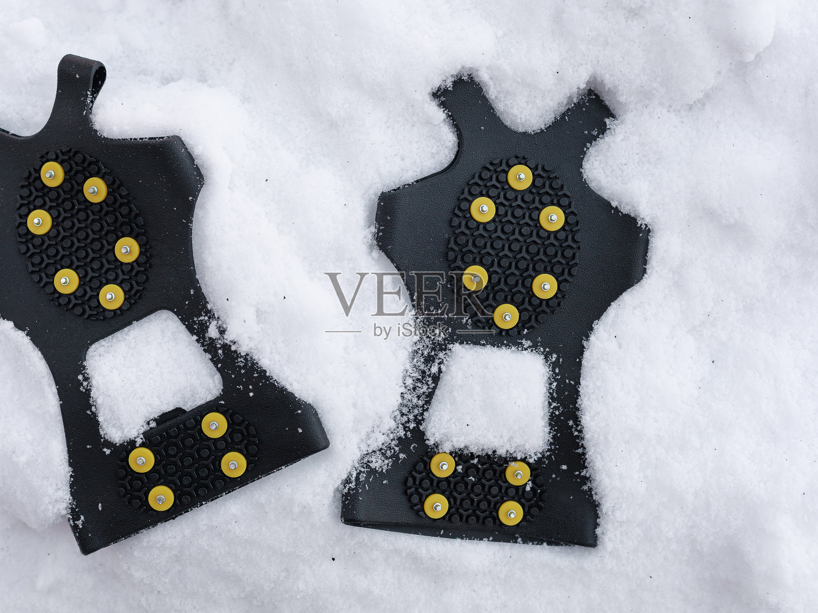 覆盖着雪的防滑冰爪,在结冰的地面上。冬季危险预防、寒冷天气装备、户外安全背景概念。照片摄影图片