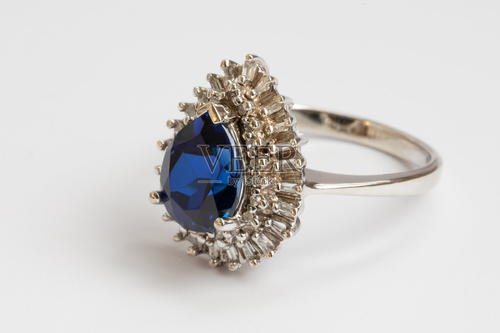 该戒指为白金材质,镶嵌有长阶梯形切割钻石和梨形切割蓝宝石。照片摄影图片