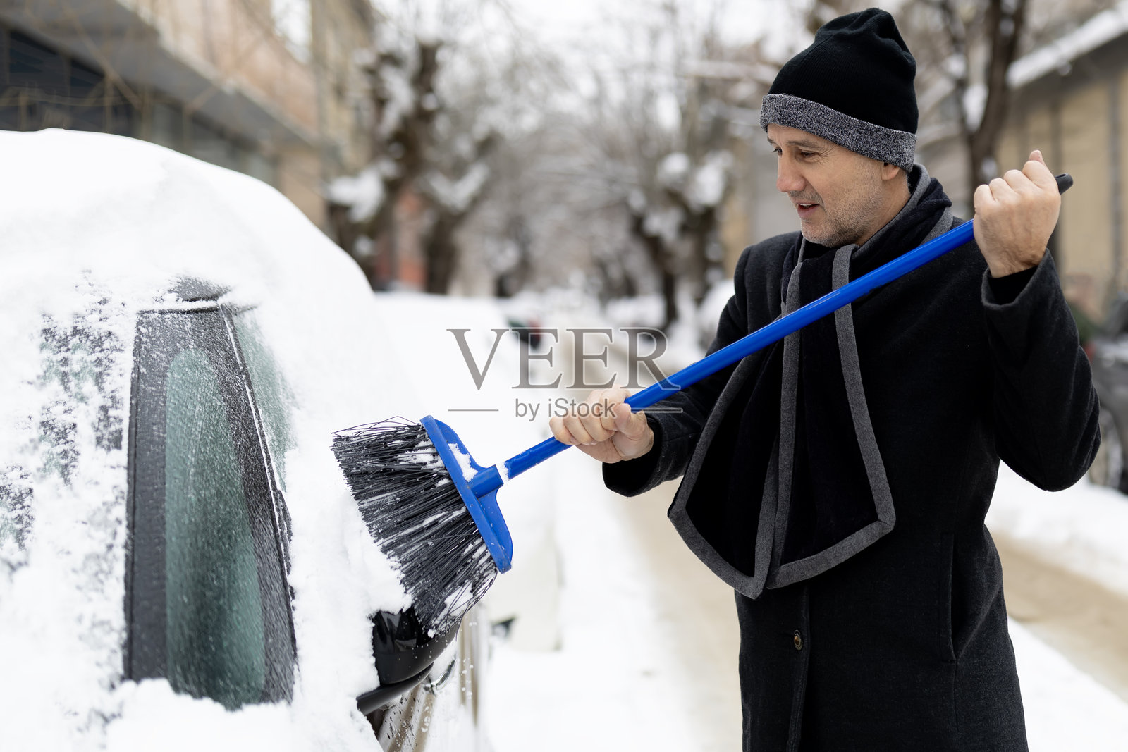 冬日降雪后,一名男子正在清理汽车上的积雪照片摄影图片