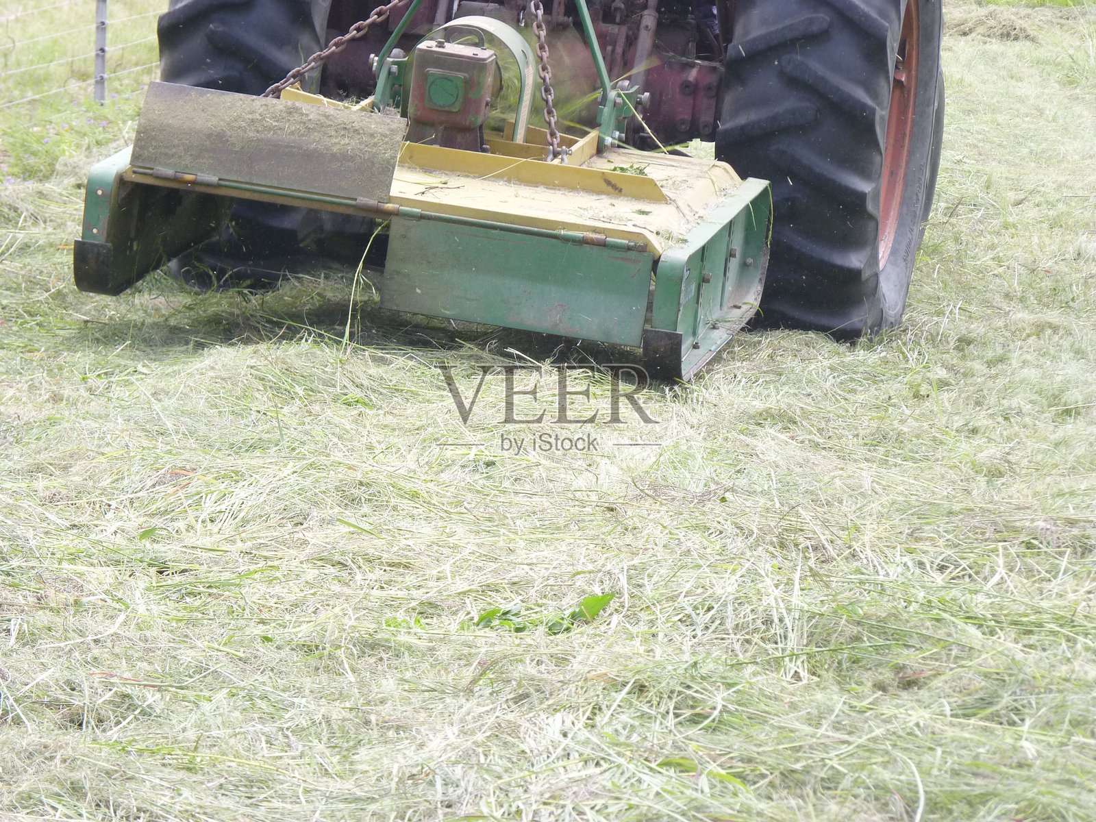 拖拉机后视镜,其车轮牵引割草机在田野里切割牧草,成千上万的草屑颗粒散落在空中。照片摄影图片