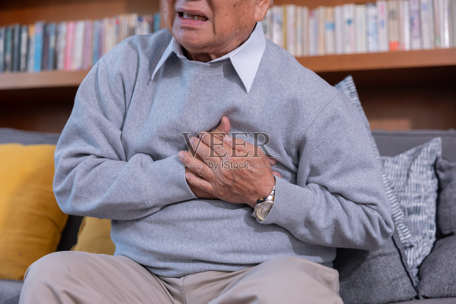 一位老人躺在客厅的地板上,用手抓住胸部,痛苦地呻吟着照片摄影图片