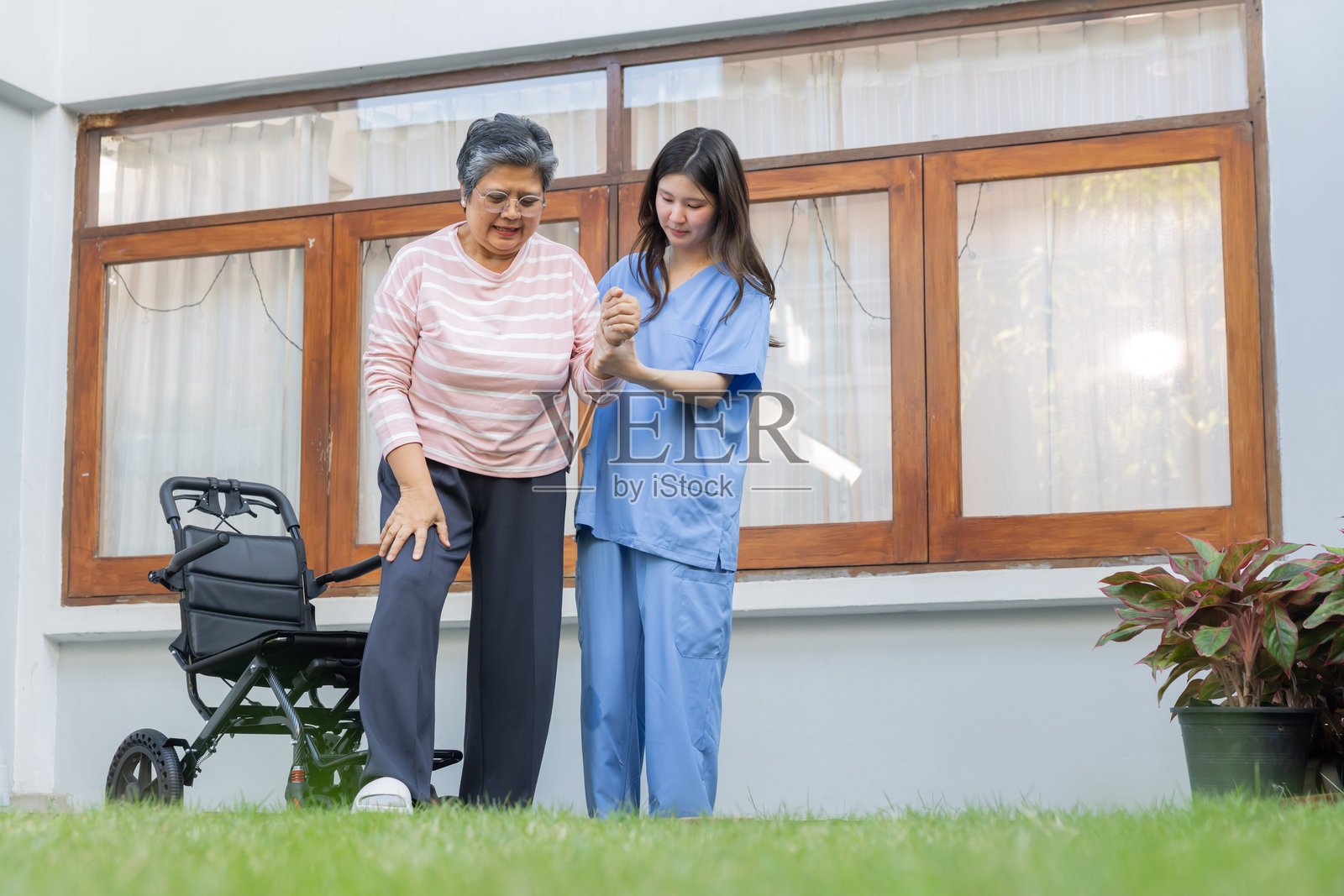 一位看护者帮助一位老年妇女在草地上行走照片摄影图片