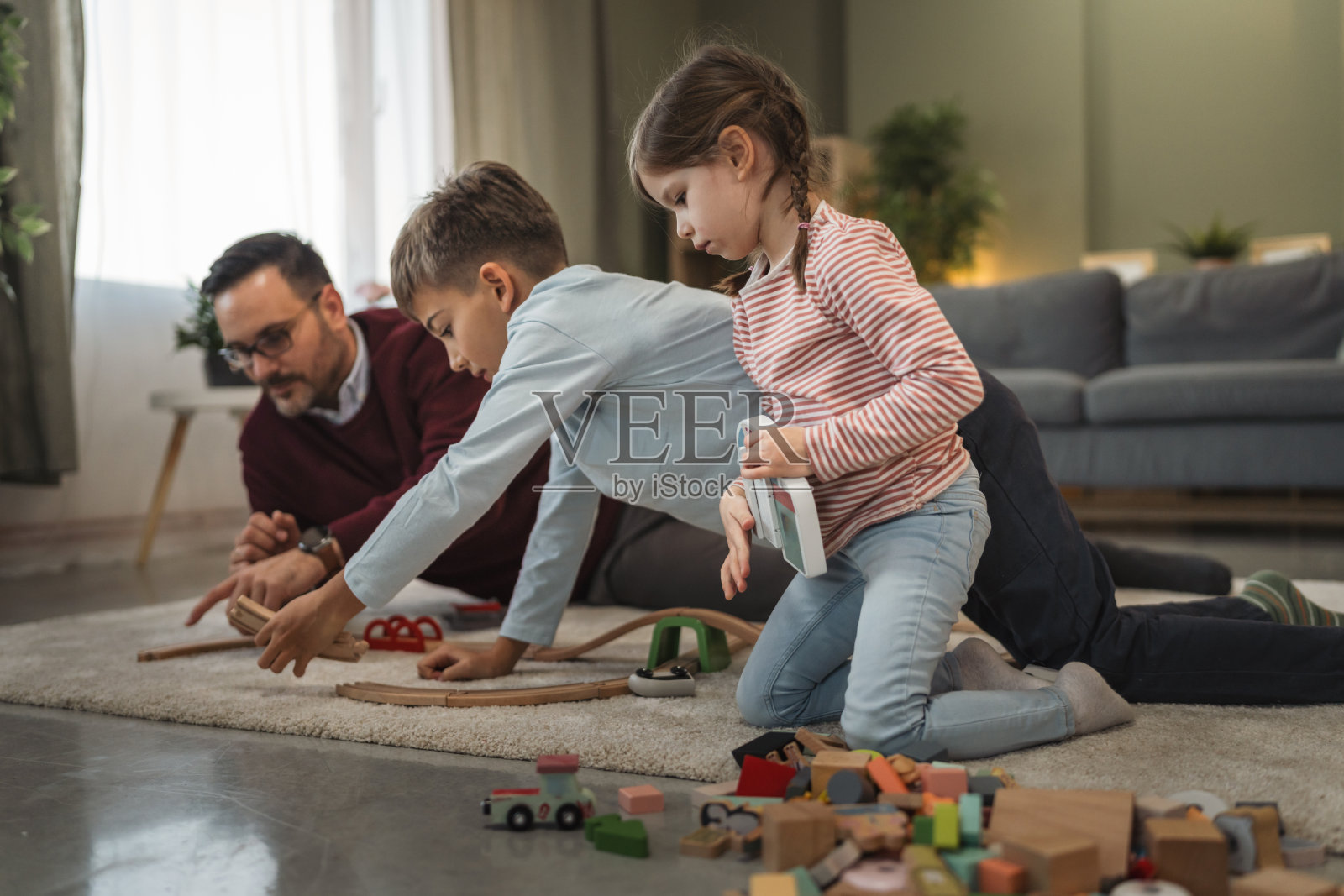 父亲在地毯上和儿子女儿玩木制火车照片摄影图片