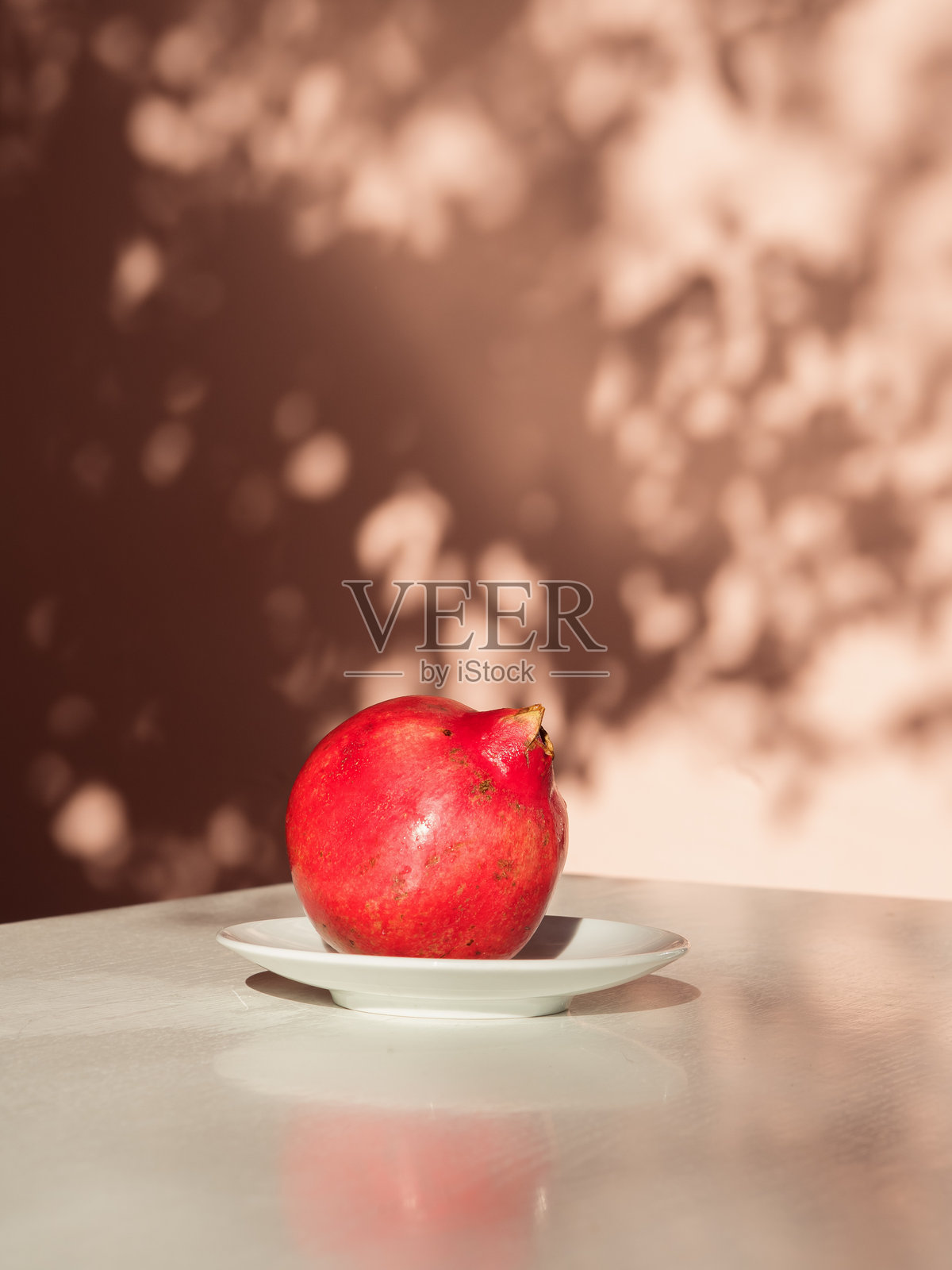 浅色墙壁上的花卉阴影,盘子里的成熟石榴,极简静物照片摄影图片