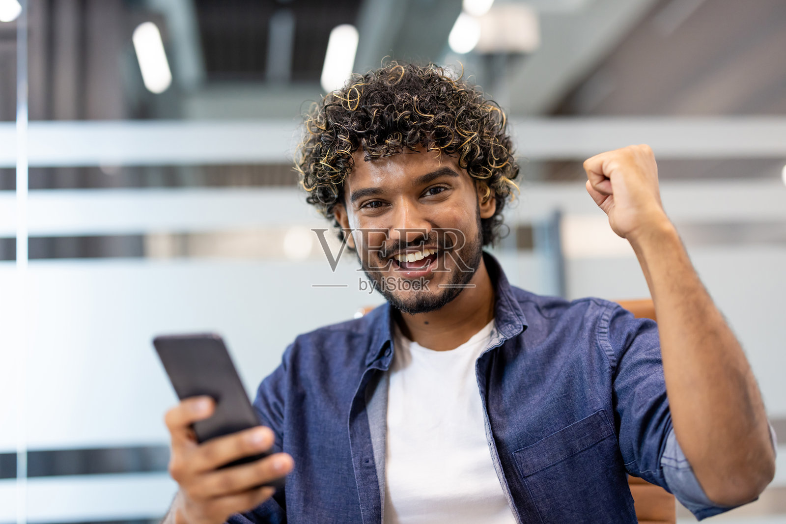 一位年轻印度男子手持手机,在镜头前为好消息和成功而欢欣鼓舞的特写肖像照片摄影图片