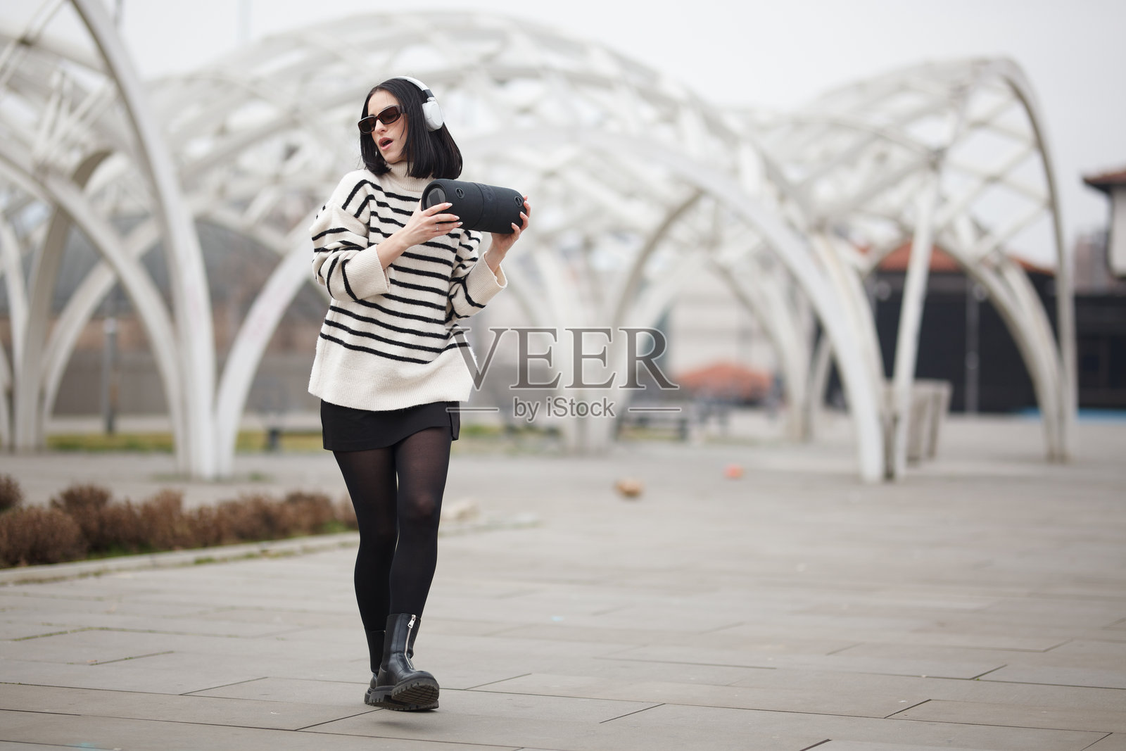 阴天,年轻女子在现代户外空间里尽情舞动,手持音乐设备,展现创意与自我表达照片摄影图片