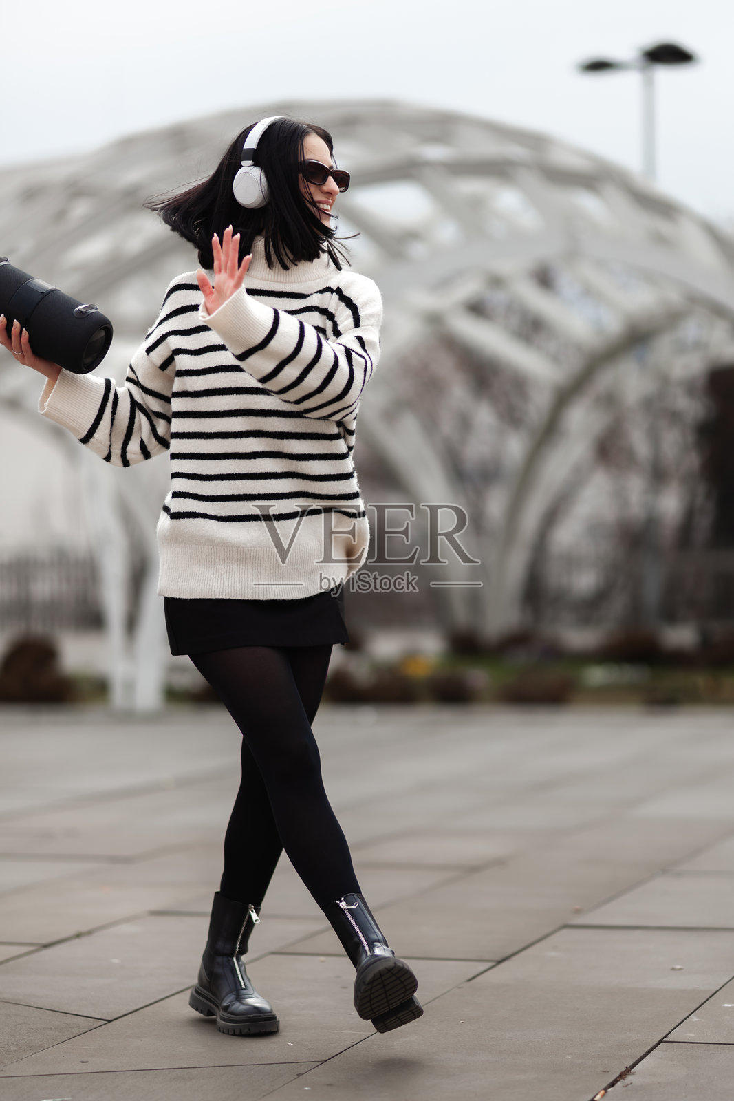 一个女孩在阴天戴着耳机,穿着时尚的条纹毛衣,在户外快乐地跳舞照片摄影图片