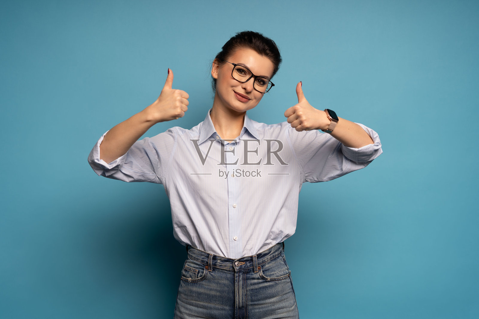 正面照:一位竖起大拇指的积极女性,在蓝色背景下孤立。照片摄影图片