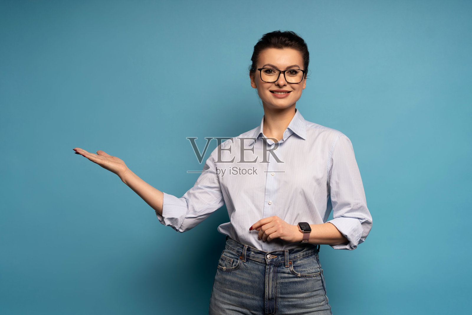 一位穿着蓝色衬衫的快乐女商人,对着镜头伸出手指,正在展示广告优惠,她孤立地站在蓝色的背景上。照片摄影图片