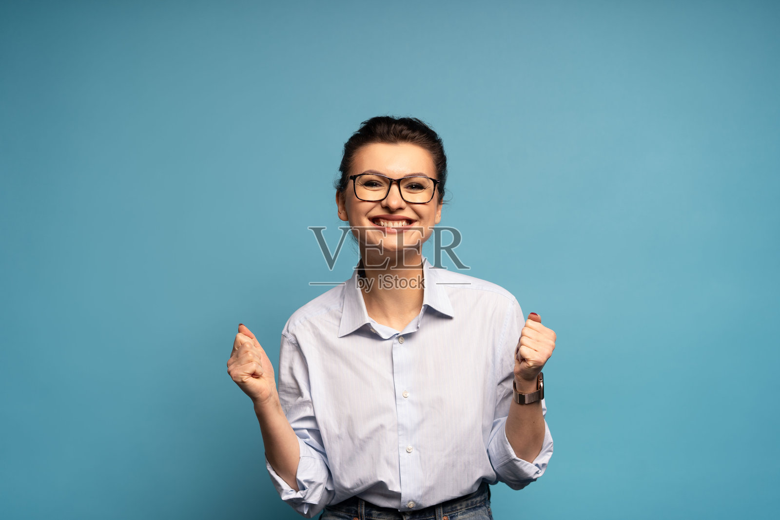 一名非常开心的女子,高举握紧的拳头站着,像是中了彩票、庆祝成功,在蓝色背景下被孤立出来照片摄影图片