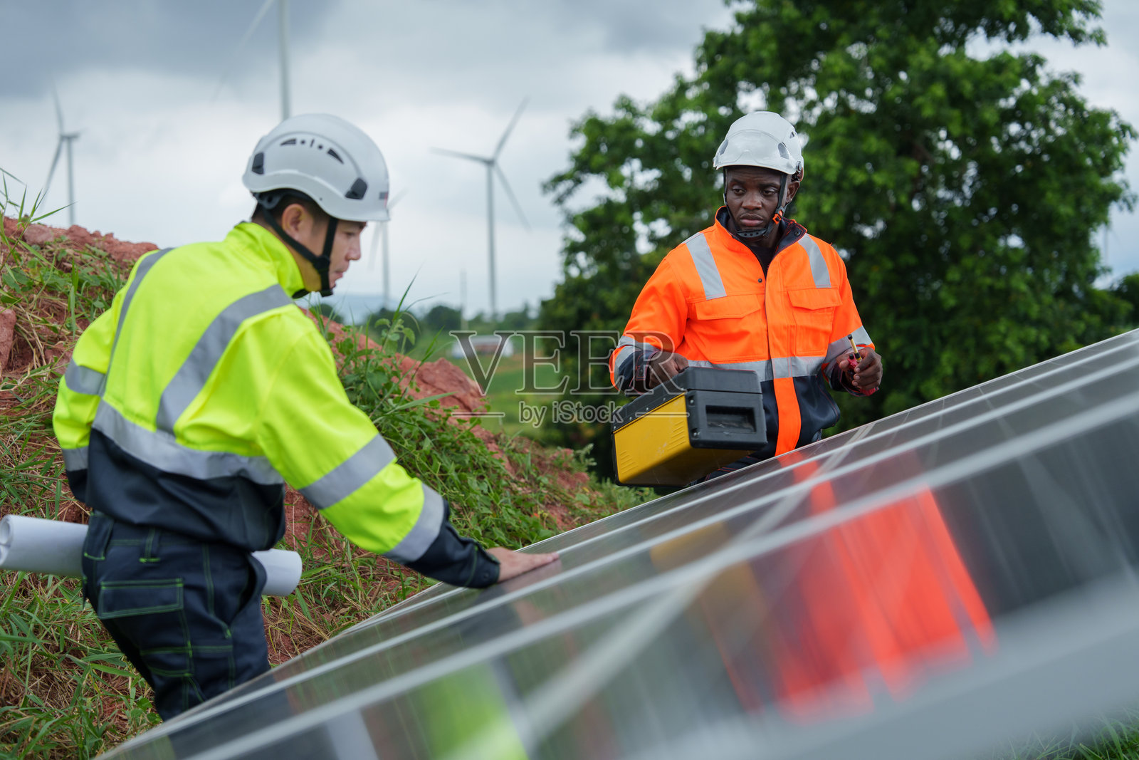 太阳能工程师在发电厂和风力涡轮机外部,对太阳能电池板的性能进行咨询和检查。照片摄影图片