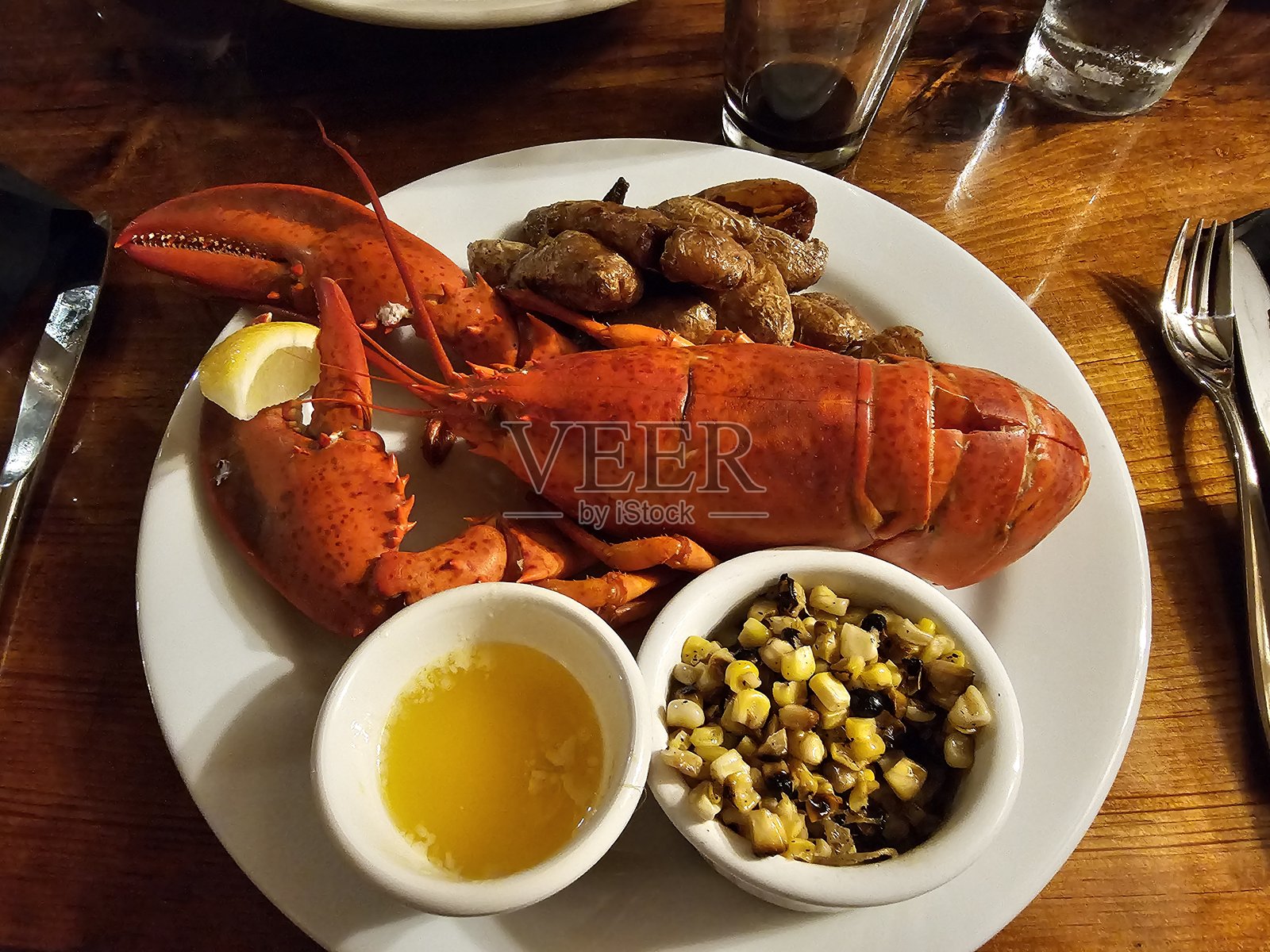 餐厅餐桌上,晚餐餐盘里盛放着一整只煮熟的龙虾海鲜及配菜。照片摄影图片