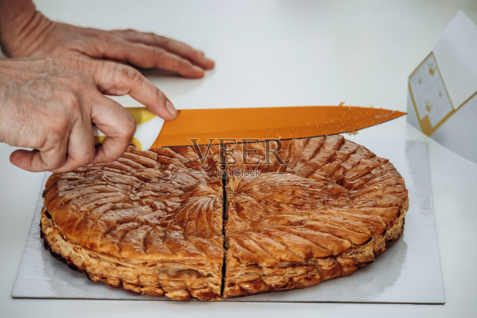 一位女士正在切“国王饼”(Galette des Rois),这是一种传统的法式酥皮糕点,内含杏仁奶油,通常在一月分享以庆祝主显节和三王节的传统。照片摄影图片