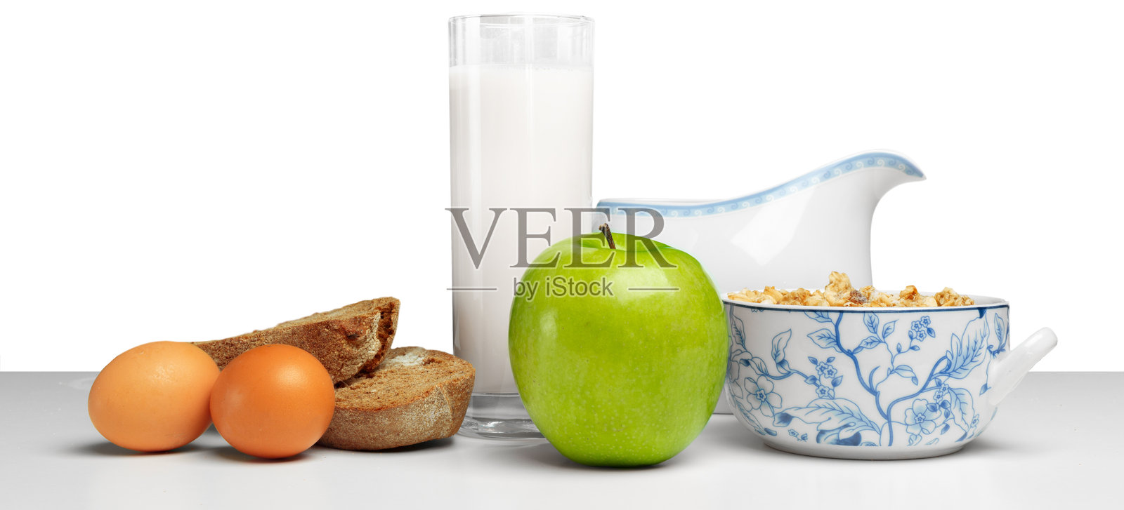 干净的桌子上摆放着丰盛的健康早餐,包括鸡蛋、青苹果、牛奶和零食。照片摄影图片