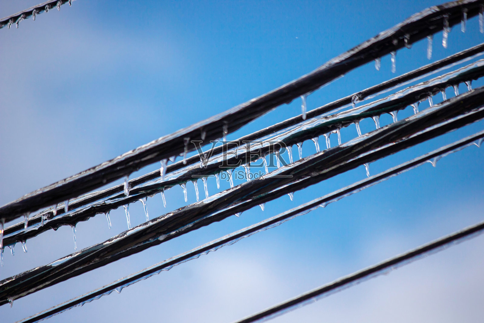 冰冻雨水导致电线上挂满冰柱,背景是蓝天照片摄影图片