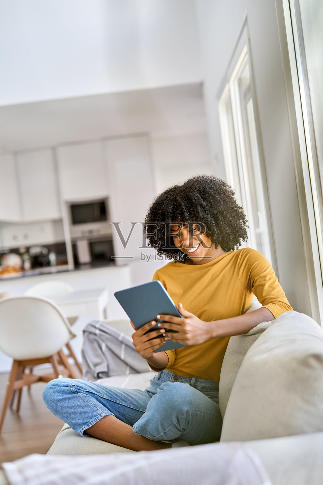 快乐的年轻非裔美国女性在家中坐在沙发上使用平板电脑。照片摄影图片