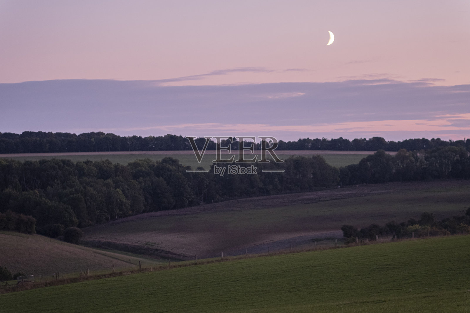 英国科茨沃尔德美丽绿色山丘上的日落黄昏风景,伴有月光照片摄影图片