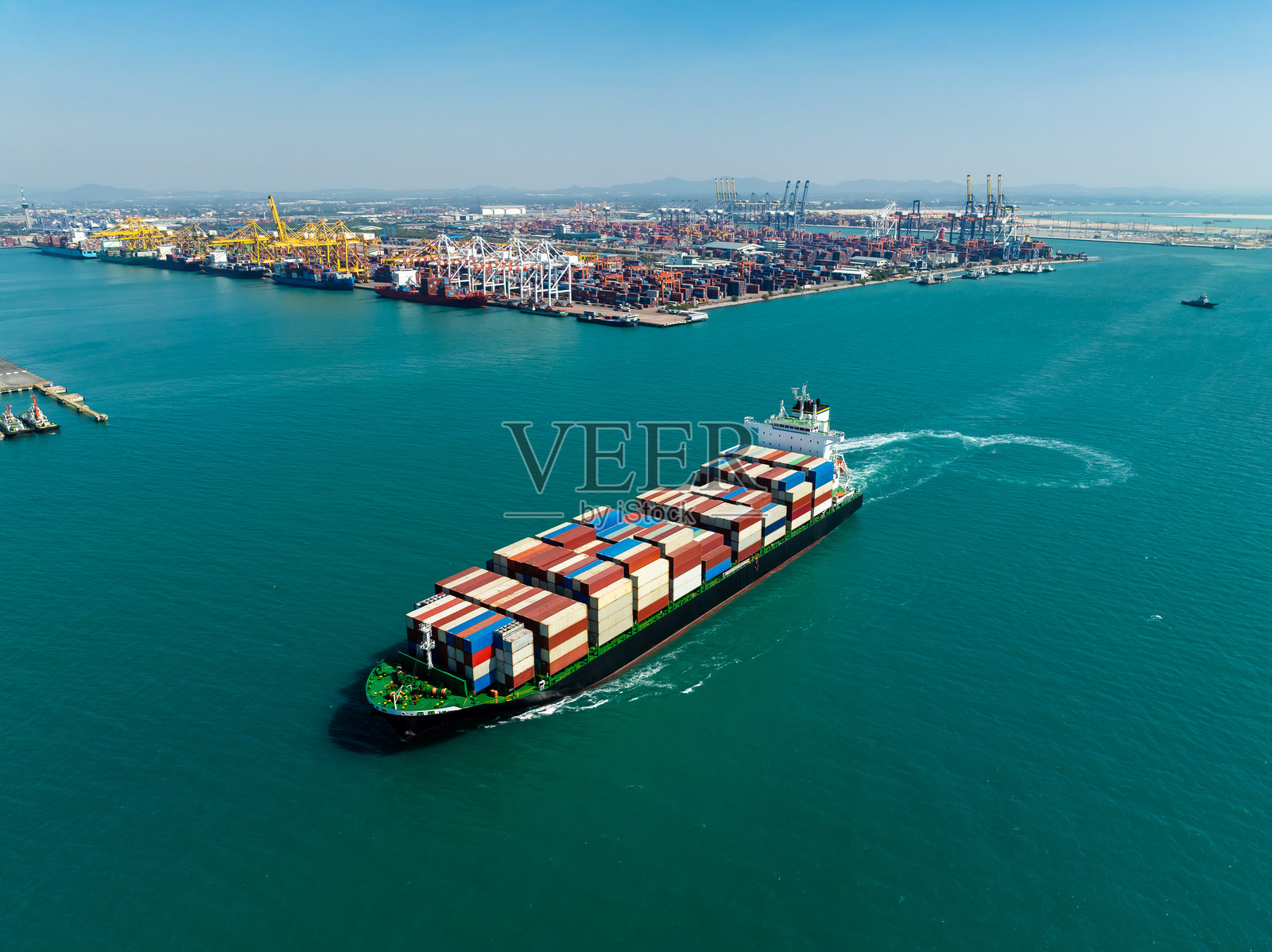 集装箱船接近繁忙工业港口枢纽的航拍图,象征经济发展照片摄影图片