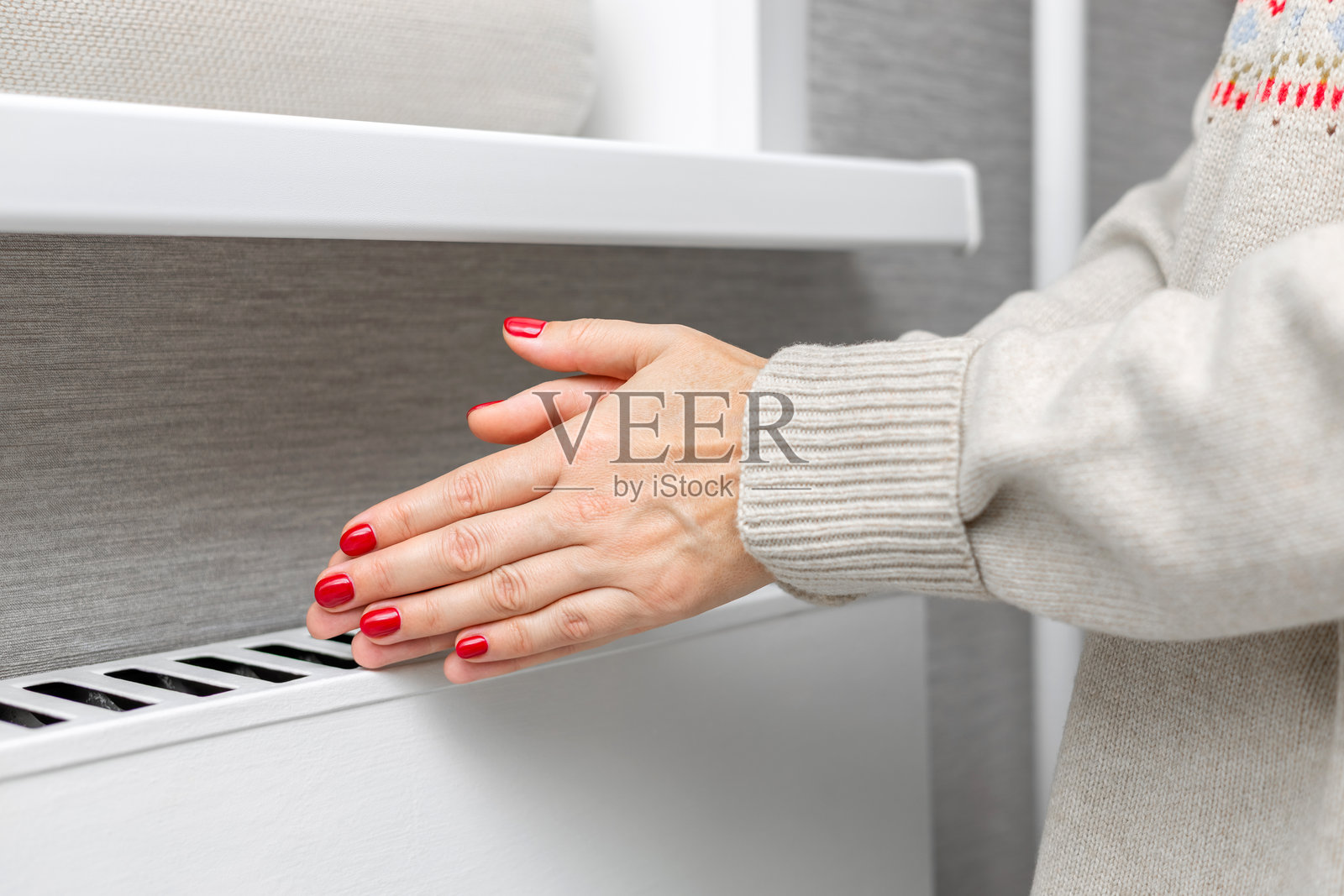 一个穿着针织毛衣的女孩在暖气旁暖手。照片摄影图片