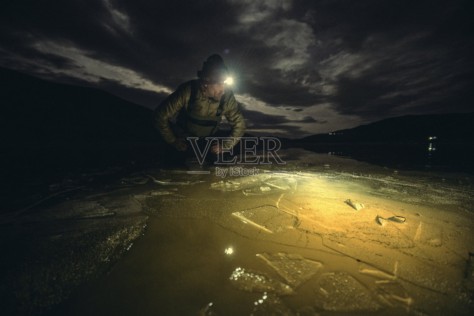 夜间户外。一位老年男子戴着头灯探索冰冷的水域照片摄影图片