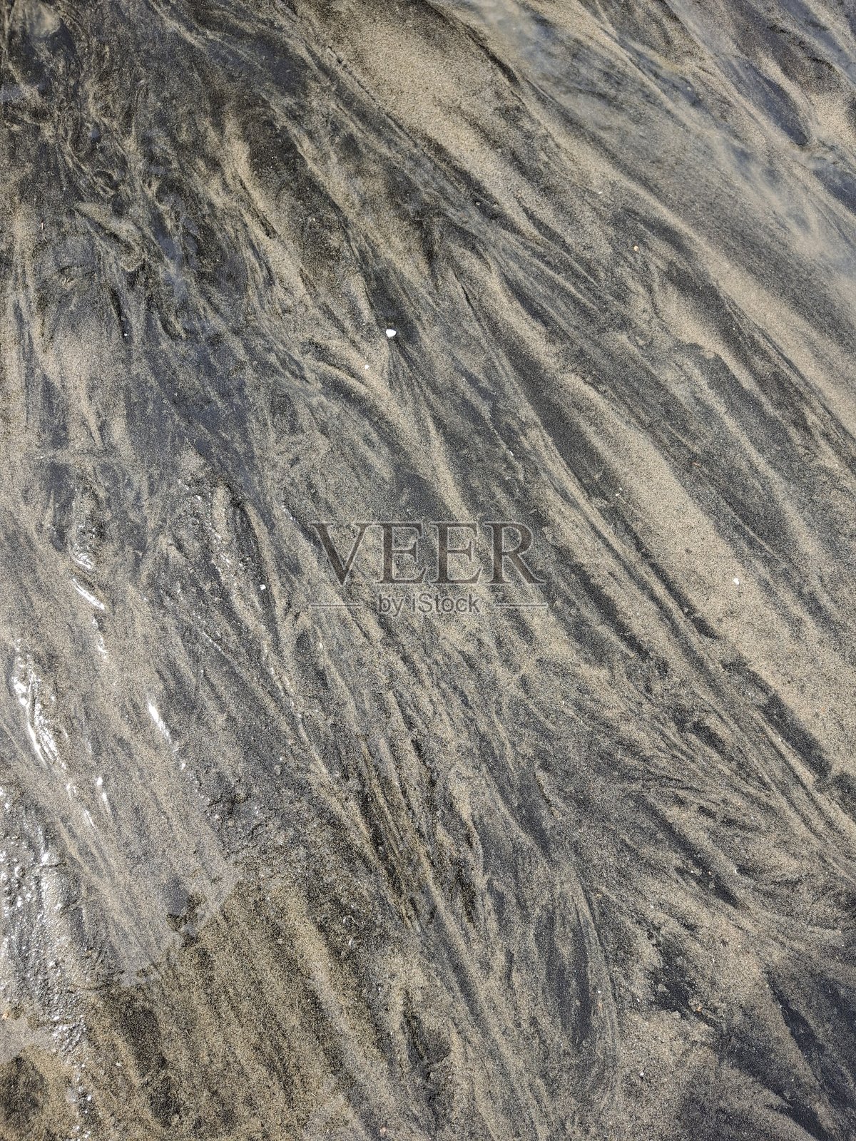 沙滩上湿沙形成的有趣深浅纹理背景,图像展示了海滩上湿沙因水流形成的波浪纹理和沉积图案。照片摄影图片