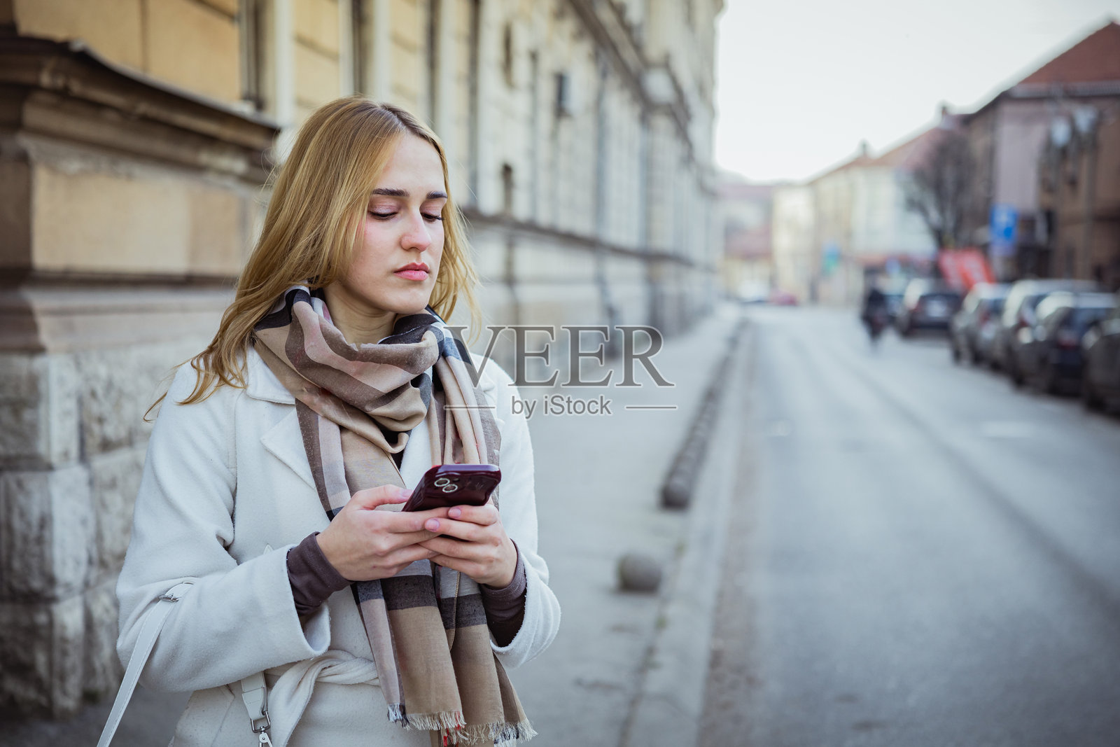 一位年轻漂亮的商界女性在寒冷的冬日街头,在等待网约车时使用手机上的打车软件。这位女性游客正在等待出租车,准备探索这座新城市。照片摄影图片