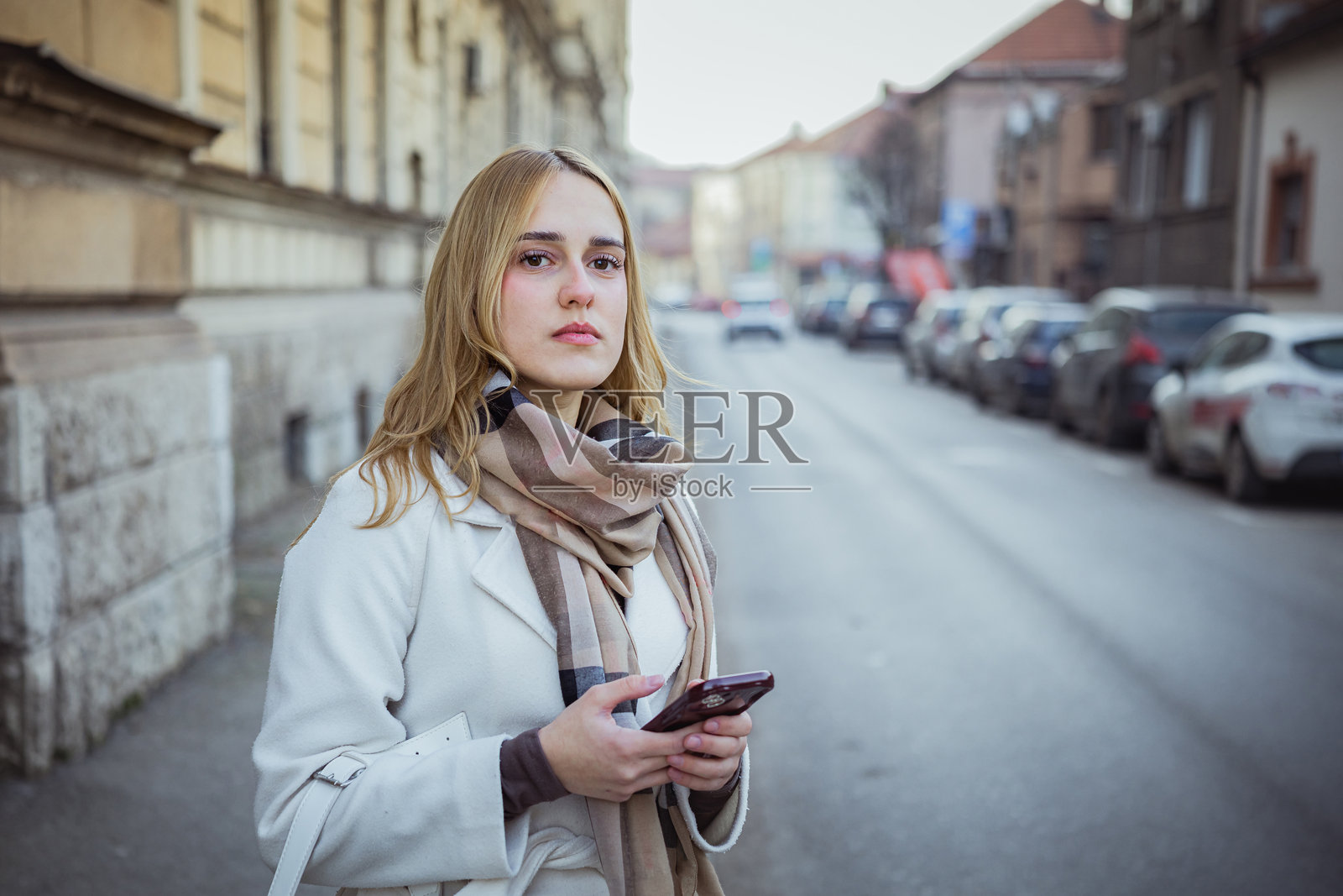 一位年轻漂亮的商界女性在寒冷的冬日街头,在等待网约车时使用手机上的打车应用。一位女性游客在等待出租车,准备探索新城市。照片摄影图片