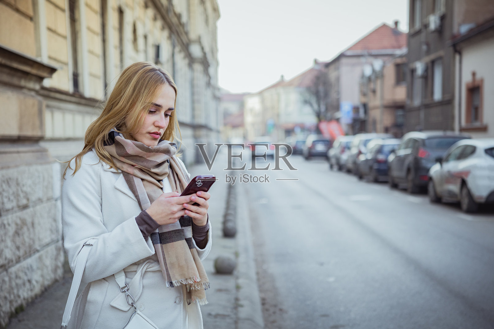一位年轻漂亮的商界女性在寒冷的冬日街头,在等待网约车时,正在使用手机上的打车应用。一位女游客在等待出租车,准备探索新城市。照片摄影图片