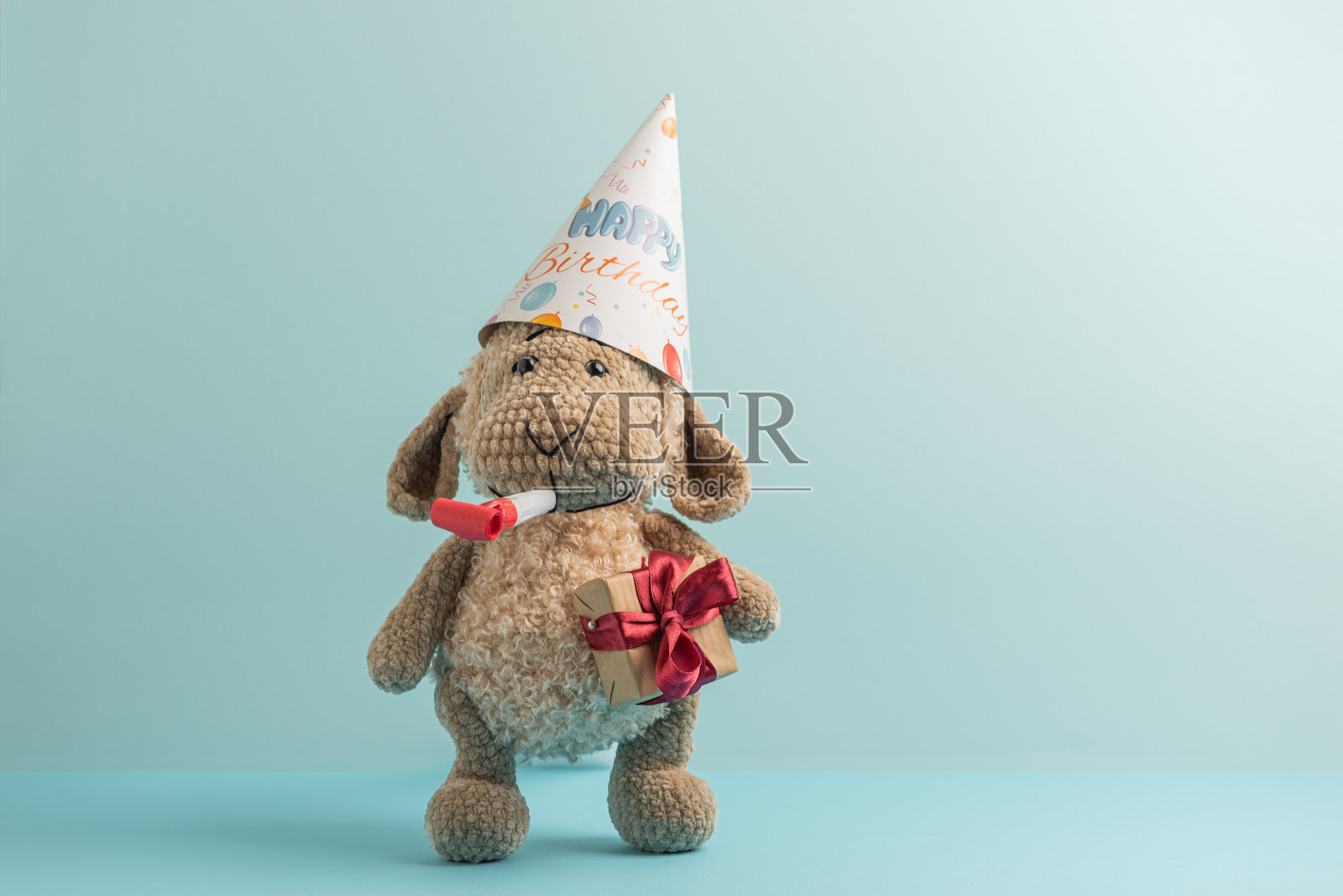 戴着生日帽的毛绒玩具羊,配有礼物和派对喇叭。节日贺卡照片摄影图片