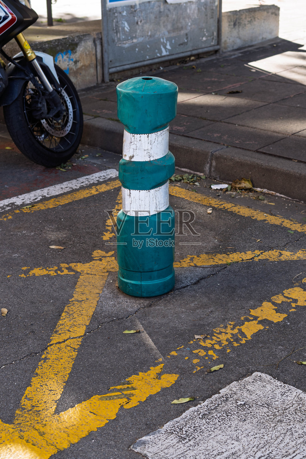 一个塑料的绿白相间的安全柱,立在沥青地面上,地面上有黄色的交通标线,背景中有一辆摩托车。照片摄影图片