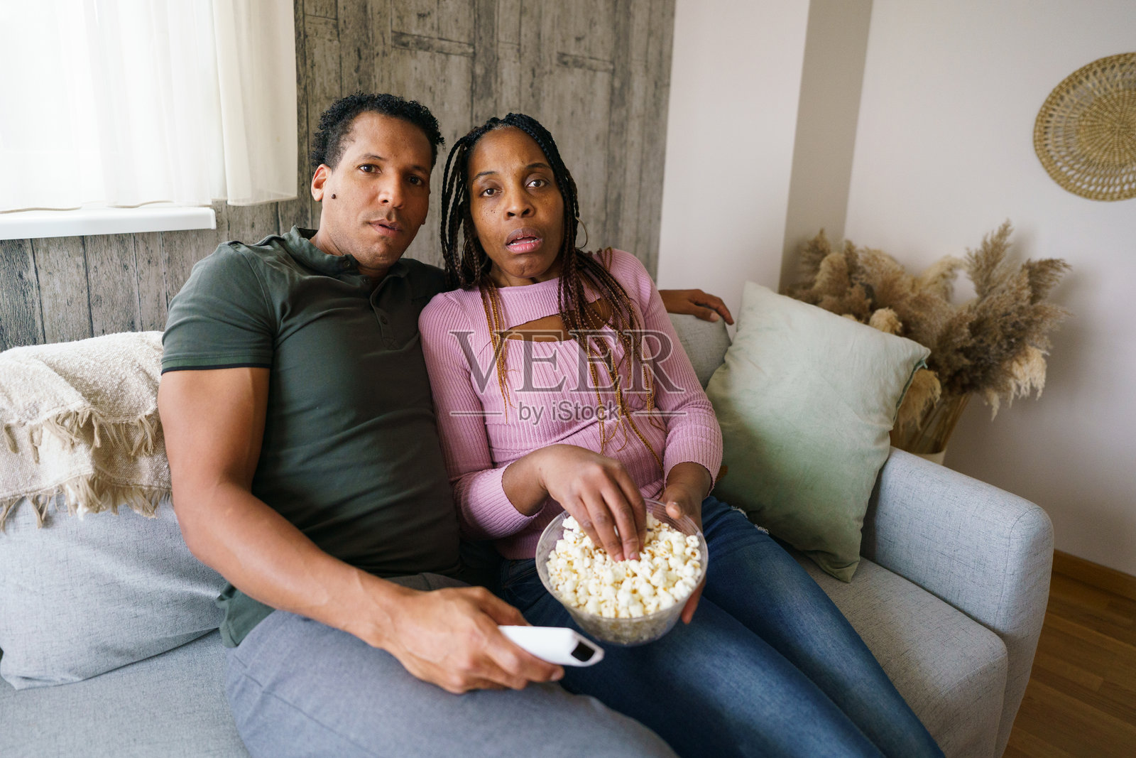 情侣边看电视边吃爆米花,表情紧张又震惊。照片摄影图片