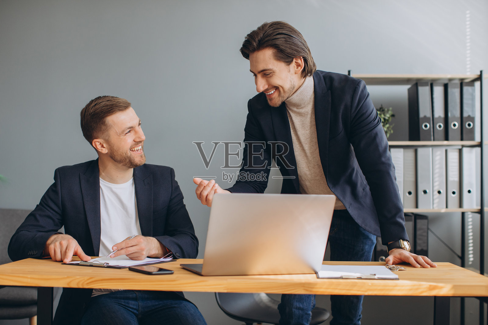 两位同事在现代办公室的笔记本电脑前微笑着讨论业务,合作开展项目照片摄影图片