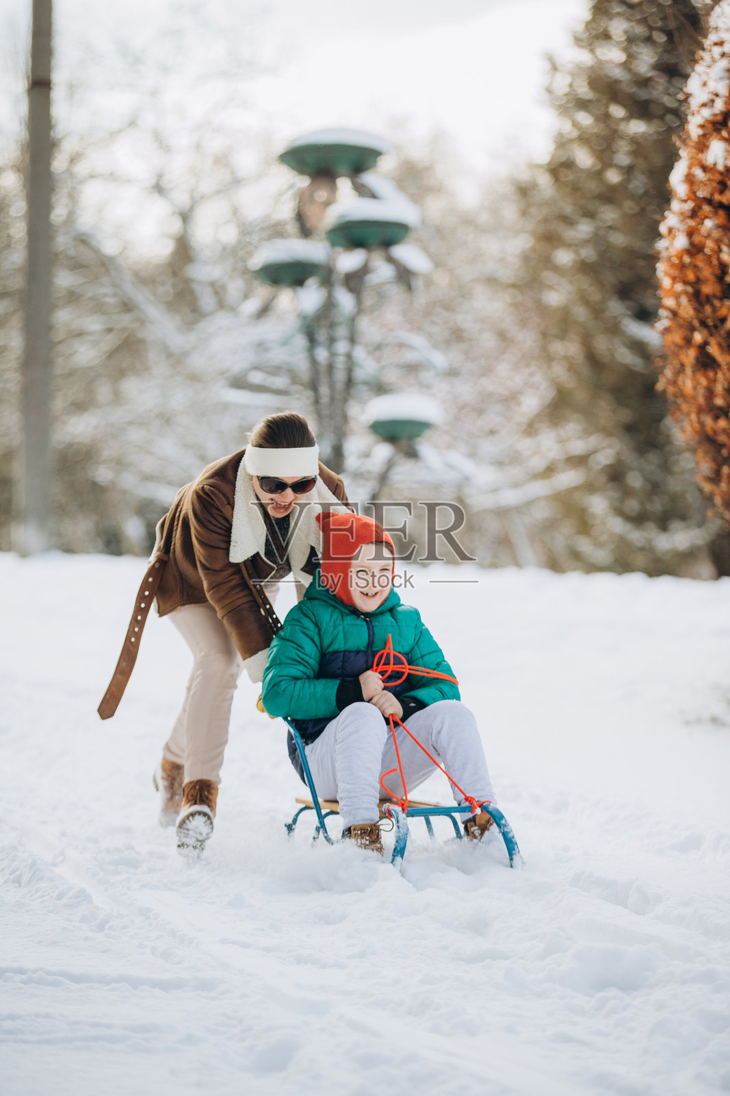 妈妈在冬天的公园里推着儿子在雪橇上照片摄影图片